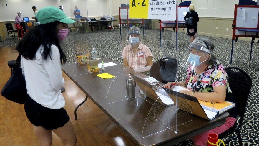 Election workers wear masks and face shields and work behind plexiglass while assisting a voter during Maine's primary elections on July 14 in Portland.
