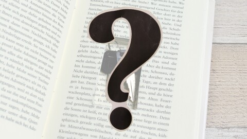 An open book with a small rectangle cut out of the pages, keys within; a black question mark in the foreground