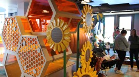 A giant honeycomb structure stands inside a room, with kids playing behind and parents standing. 