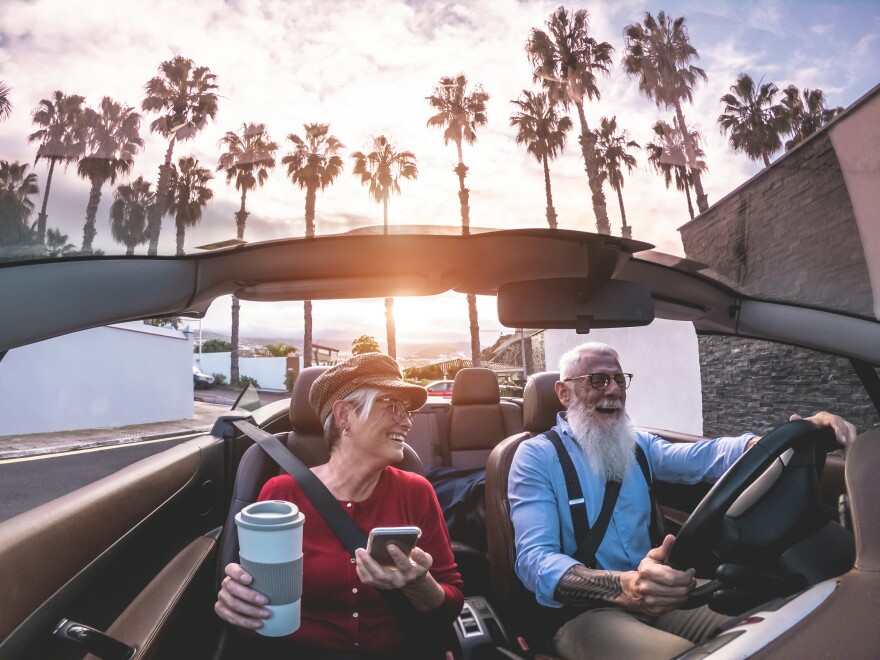 A senior couple inside a convertible car on holiday time - AAA Auto Club expects lower gas prices and record air travel