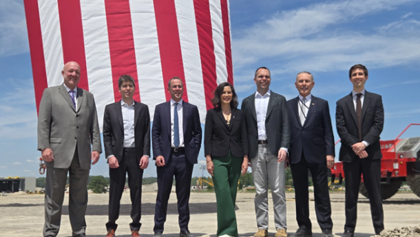 Michigan Governor Gretchen Whitmer stands alongside business leaders including OpenAI CEO Sam Altman at a groundbreaking ceremony Monday, framed by a massive American flag.