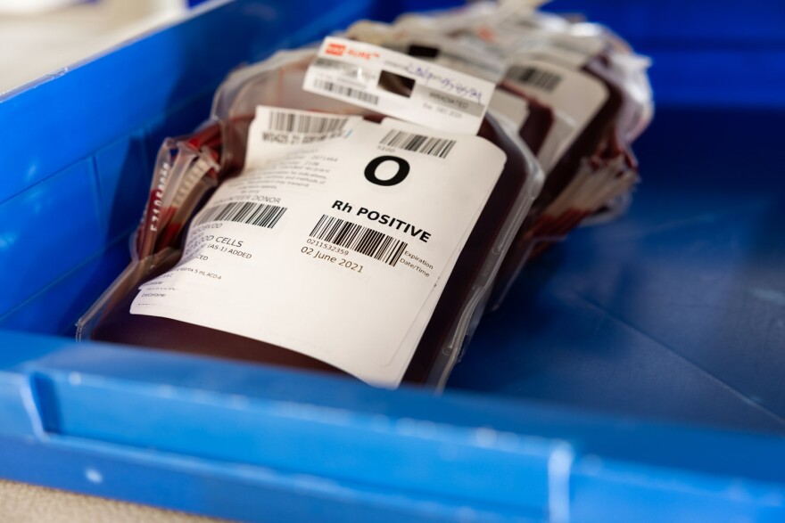 Bags of blood sit in a blue plastic container. The top one has a visible label that says O positive. 