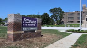 A brick sign in front of a brick school building. A section of the sign is purple and says Pittsburg Community Middle School.