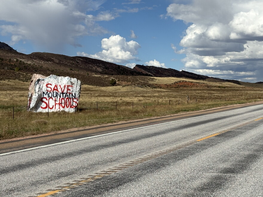 A rock, painted white, sits off to the side of an empty highway. 