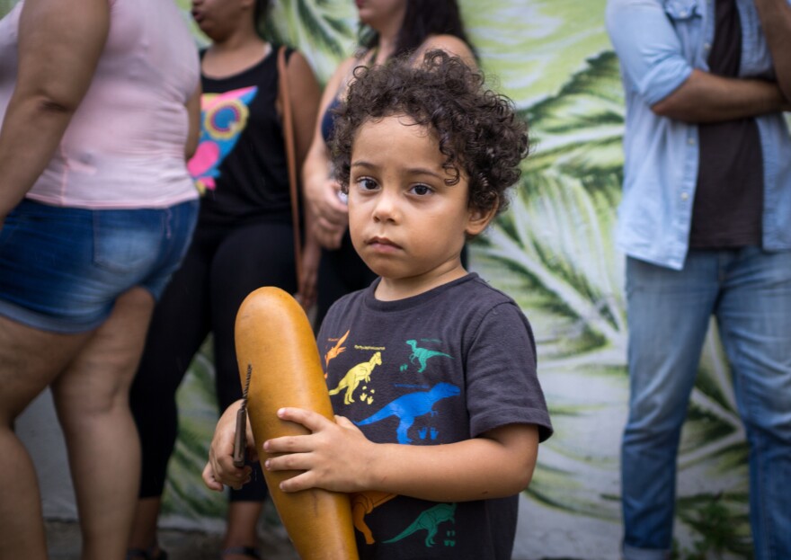 Tito Matos' son Marcelo Matos Reyes, 3, holds a guiro, a percussive instrument, as part of the Plena.