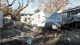 A mobile home damaged with debris in the foreground