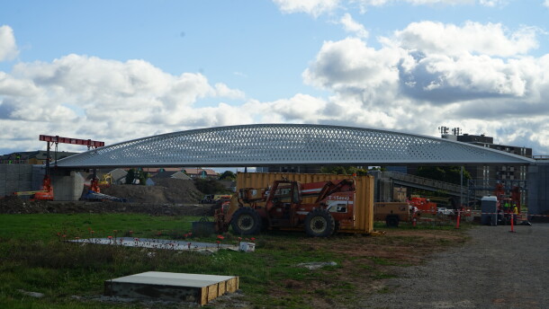 A grey pedestrian bridge installed on a construction site with a blue sky and white clouds. 