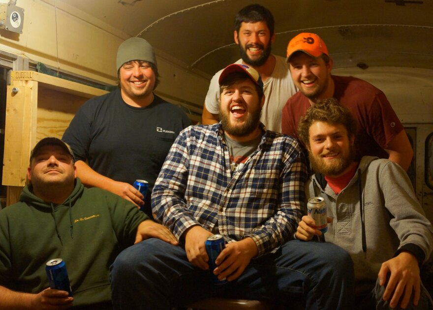 Six young men drinking beer in an old schoolbus, laughing