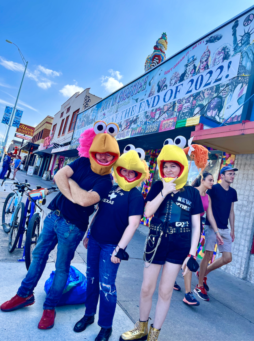 Three people pose on the sidewalk outside a store wearing Muppet heads.