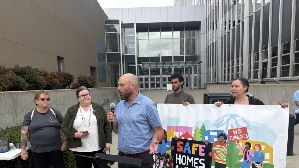 People stand at a press conference in front of a Tacoma court house. They have a banner that reads "Safe Homes For All" 