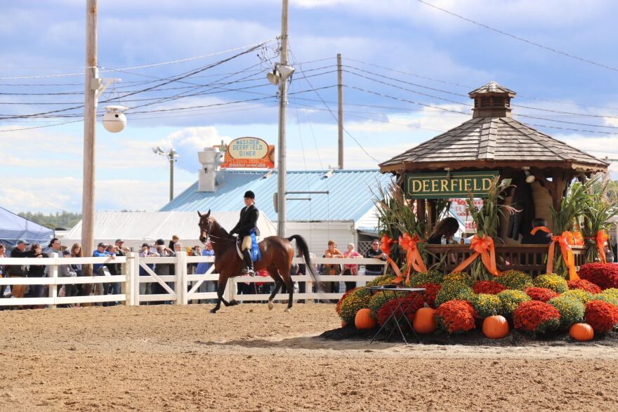 A competitor wearing a blue ribbon rides a horse around the outdoor arena at the Deerfield Fair in 2021.