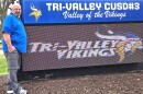 Tri-Valley football coach Josh Roop stands next to an electronic sign that reads 'Tri-Valley Vikings' and features a blue and gold colored Viking mascot  