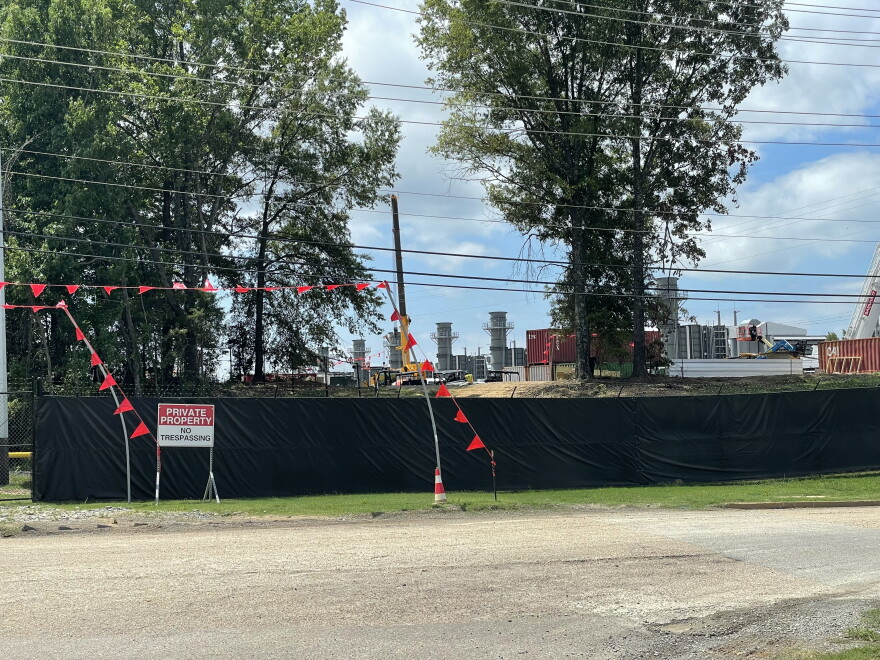 A black fence with a sign that reads "Private Property -- No Trespassing" stands in front of a property that contains smoke stacks, shipping containers and other industrial equipment. 