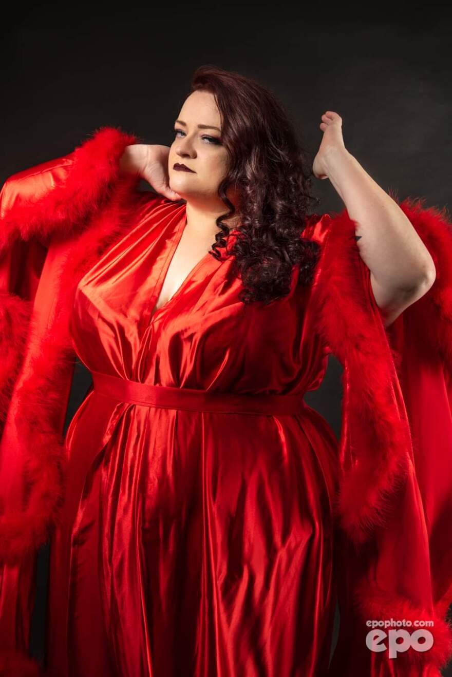 A woman poses dramatically in a silk dress and feather boa.