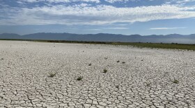 Desiccated, cracked earth surrounding the Great Salt Lake. There are mountains in the distance and white clouds on a blue sky. 