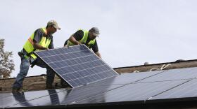 Workers install a rooftop solar panel on a home.