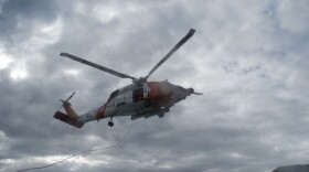 A white and grey coast guard helicopter over cloudy skies
