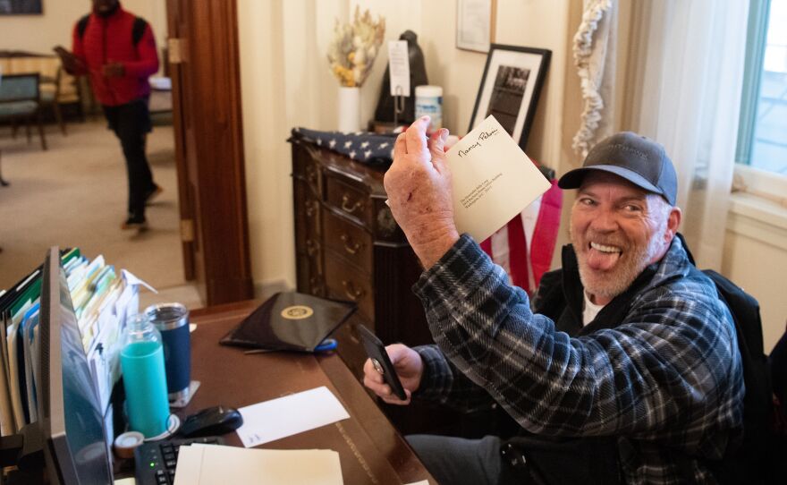 Richard Barnett holds a piece of mail as he sits inside the office of House Speaker Nancy Pelosi after rioters breached the U.S. Capitol. He bragged about leaving a note containing a sexist slur for Pelosi.