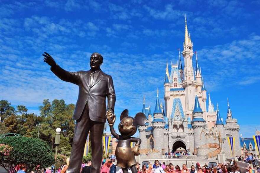 A statue of Walt Disney holding the hand of Mickey Mouse in front of Cinderella's castle at the theme park in Orlando