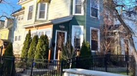 A three story green and white Stick style home in central Syracuse has wrought iron and cobble stone fencing.