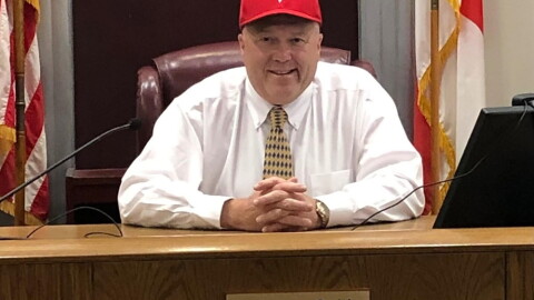 Judge Layne Smith wears a ball cap and sits in his courtroom, smiling for the camera
