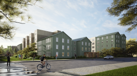 A digital rendering shows multiple teal and brown five-story buildings, surrounded by grass, trees, and blue sky. 