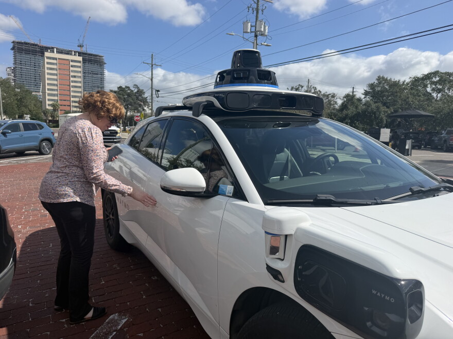 A woman takes her right hand, about to open the white Waymo car's passenger door.