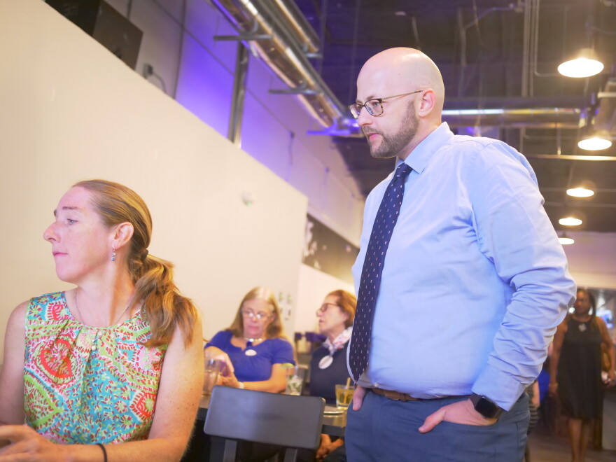 A man in a light blue shirt and dark blue tie looks over the shoulder of a woman in a colorful paisley top as they monitor the latest election results.