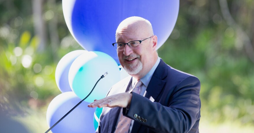 Gainesville Mayor Harvey Ward wears a suit and tie speaking into a mic with balloons in the background 