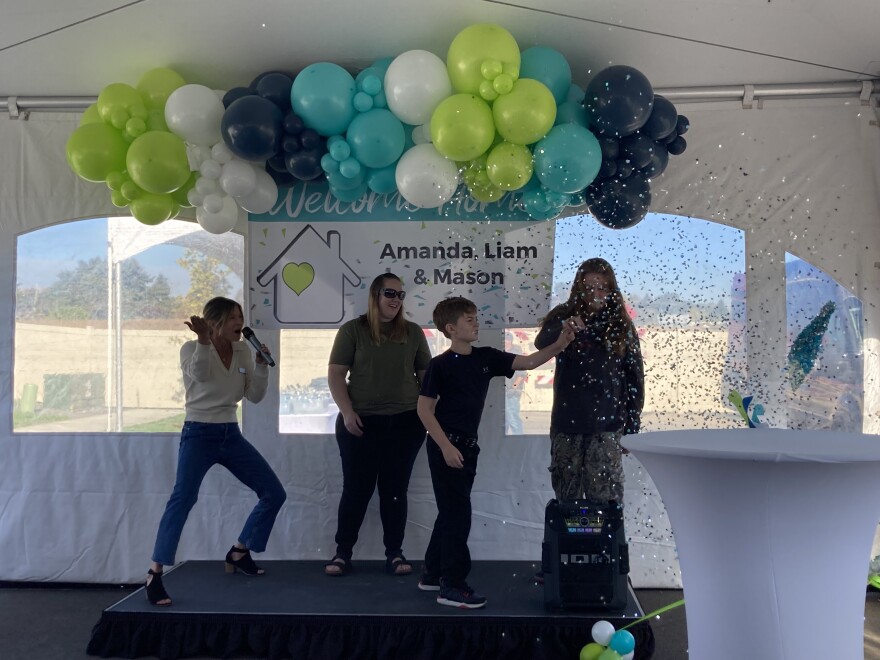 Amanda Cole and her sons Liam and Mason pop a confetti filled balloon to find the keys to their new house, surrounded by Hayden Home employees and others who helped make their homeownership possible.