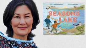 A woman with dark hair, wearing a colorful shirt, poses with her book titled "Seasons by the Lake."