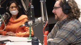 Two people sitting inside a radio studio are sitting in a radio studio. The man at right, Tom Meyer, is talking while Lisa Ray, left, is listening.