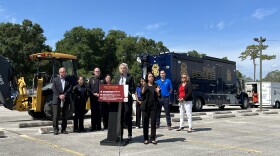  Several emergency officials for the city of tampa speaking in a parking lot in front of a podium, with emergency vehicles behind them. 