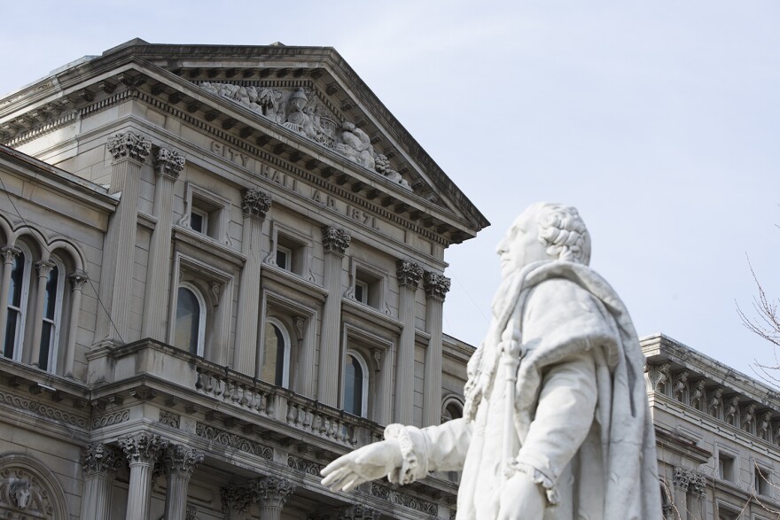 A white marble statue of Louis XIV facing left, in front of City Hall