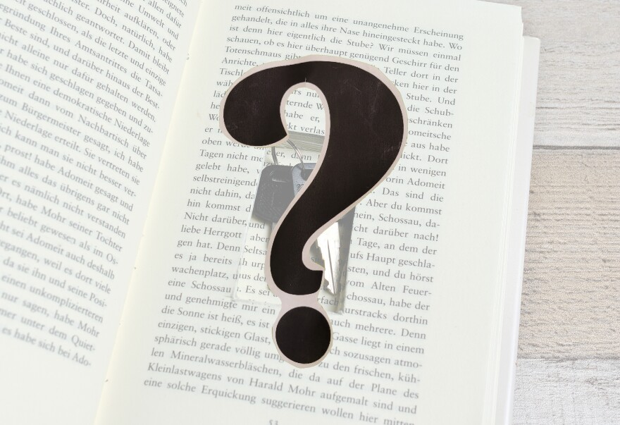 An open book with a small rectangle cut out of the pages, keys within; a black question mark in the foreground
