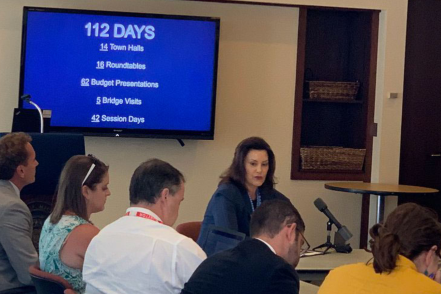 governor gretchen whitmer sitting at table with blue screen behind her