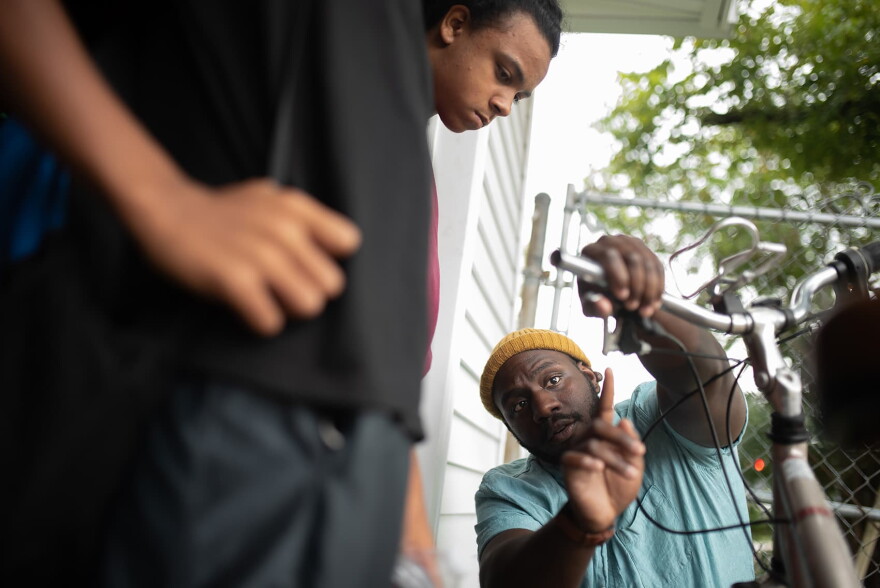 Theon Lee, right, spends time with Dorian Jones, 13, (not pictured) and Jayden Holland, 14, left, teaching them about the brakes on a bicycle at The Biker Boyz & Girlz Shop in Indianapolis. (Lucas Carter for Here & Now)