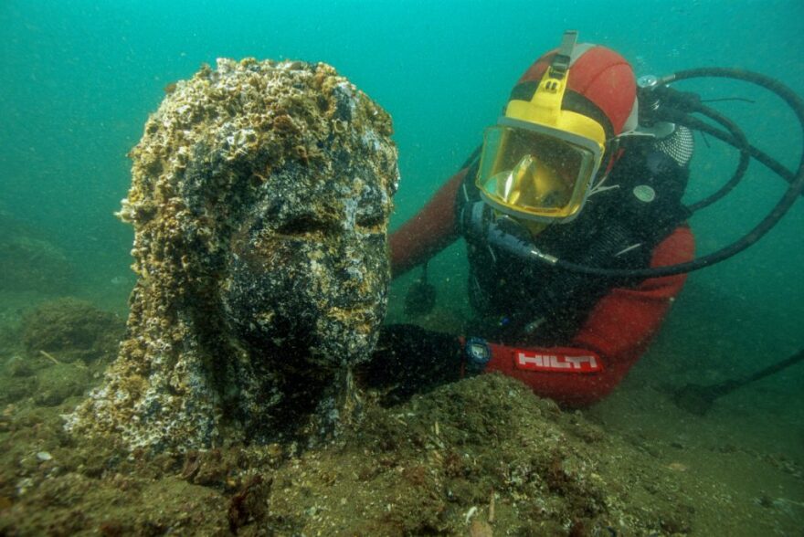 An archaeologist inspects the head still encrusted of a black stone queen on site underwater in Thonis-Heracleion, Egypt; Ptolemaic Period; granodiorite; height: 86 5/8 inches; National Museum, Alexandria (SCA 283), IEASM Excavations