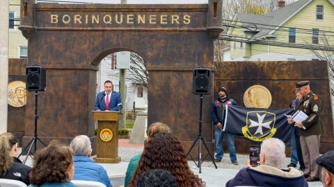 New Britain Mayor Bobby Sanchez opens the city's National Borinqueneers Day celebration on April 13, 2026. Nearby, Borinqueneers Motorcycle Club member Macho holds a flag with the 65th infantry regiment symbol as U.S. Sen. Richard Blumenthal and retired U.S. Army First Sergeant Juan Cruz (far right) listen.