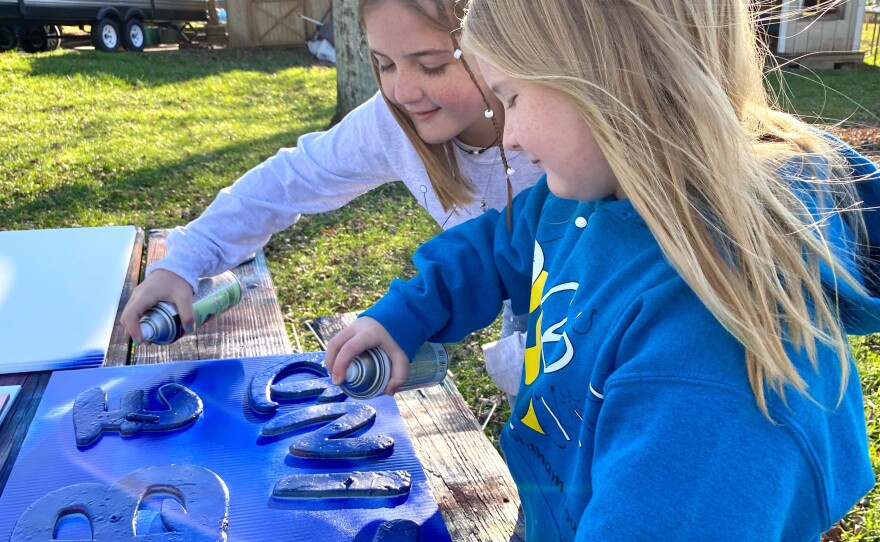 Sisters, Raegan and Rylyn Richins look closely at one of their newly painted "Be Kind" signs.
