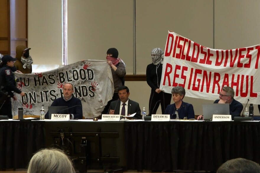 Protesters stand behind Provost Rahul Shrivastav and leader of the Bloomington Faculty Council meeting on March 25.