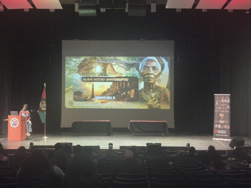 Host of the 1st Sankofa Conference Buffalo, Shantelle Patton, sits on stage preparing to introduce Emmanuel Kulu Jr.