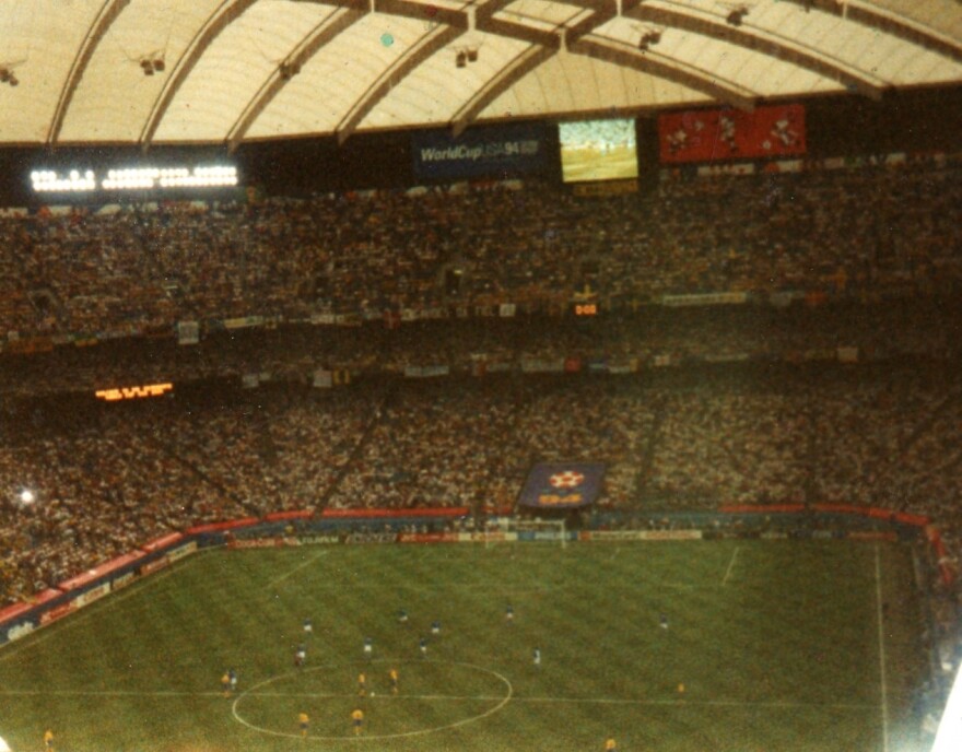 Grainy 1994 photograph of the soccer field inside the Pontiac Silverdome. The pitch is visible at the center of the stadium, surrounded by seating sections, with spectators scattered throughout the stands. 