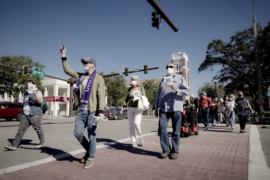 people wearing masks and holding flyers march through a city crosswalk