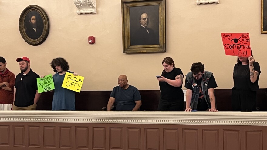 People in the balcony of the New Bedford City Council chamber held signs Tuesday as the council debated motions on the use of Flock surveillance cameras in the city.