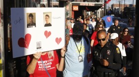 Group of people march along the street holding signs. Police officers accompany them.