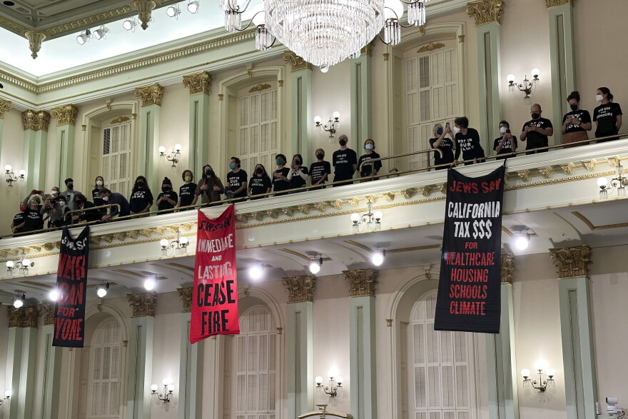 Protesters unfurl banners with messages calling for a Gaza cease fire from the upper level of the Assembly chamber.