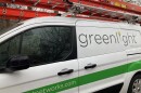 A Greenlight service truck with an orange ladder on the roof sits alongside a neighborhood street.