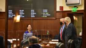 woman stands on the floor of the Legislature under a board that displays the vote count