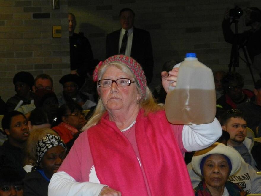 A Flint resident holds a jug containing tap water at a public meeting.